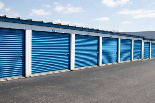 Row of blue roll-up storage unit doors along a paved drive